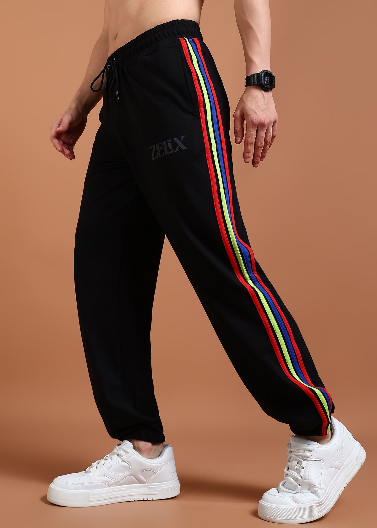 A person wearing black joggers with a multicolor stripe on the side and a drawstring waistband. The joggers have 'zelix' brand name on the left leg.